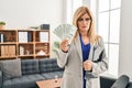 Middle age blonde woman working at therapy consultation office holding money depressed and worry for distress, crying angry and Royalty Free Stock Photo