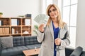 Middle age blonde woman working at therapy consultation office holding money relaxed with serious expression on face Royalty Free Stock Photo