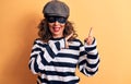 Middle age brunette burglar woman wearing mask and cap standing over yellow background smiling and looking at the camera pointing Royalty Free Stock Photo