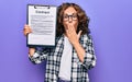 Middle age brunette business woman wearing glasses holding clipboard with contract paper sheet covering mouth with hand, shocked Royalty Free Stock Photo