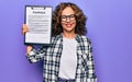 Middle age brunette business woman wearing glasses holding clipboard with contract paper sheet looking positive and happy standing Royalty Free Stock Photo