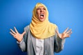 Middle age brunette business woman wearing muslim traditional hijab over blue background crazy and mad shouting and yelling with Royalty Free Stock Photo