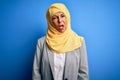 Middle age brunette business woman wearing muslim traditional hijab over blue background In shock face, looking skeptical and