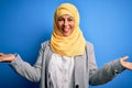 Middle age brunette business woman wearing muslim traditional hijab over blue background smiling showing both hands open palms, Royalty Free Stock Photo