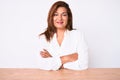 Middle age brunette hispanic business woman wearing casual white shirt sitting on the table happy face smiling with crossed arms Royalty Free Stock Photo