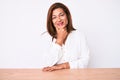 Middle age brunette hispanic business woman wearing casual white shirt sitting on the table looking confident at the camera Royalty Free Stock Photo