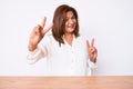 Middle age brunette hispanic business woman wearing casual white shirt sitting on the table smiling looking to the camera showing Royalty Free Stock Photo