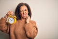 Middle age brunette woman holding clasic alarm clock over isolated background touching mouth with hand with painful expression