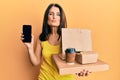 Middle age brunette woman holding take away food showing smartphone screen looking at the camera blowing a kiss being lovely and Royalty Free Stock Photo