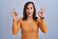 Middle age brunette woman standing wearing orange sweater looking surprised and shocked doing ok approval symbol with fingers Royalty Free Stock Photo