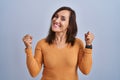 Middle age brunette woman standing wearing orange sweater very happy and excited doing winner gesture with arms raised, smiling