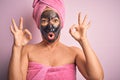 Middle age brunette woman wearing beauty black face mask over isolated pink background looking surprised and shocked doing ok Royalty Free Stock Photo