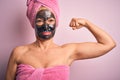 Middle age brunette woman wearing beauty black face mask over isolated pink background Strong person showing arm muscle, confident