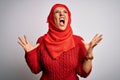 Middle age brunette woman wearing muslim traditional hijab over isolated white background crazy and mad shouting and yelling with Royalty Free Stock Photo