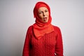 Middle age brunette woman wearing muslim traditional hijab over isolated white background In shock face, looking skeptical and