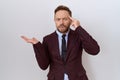 Middle age business man with beard wearing suit and tie confused and annoyed with open palm showing copy space and pointing finger
