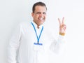 Middle age business man wearing ID card over white background smiling with happy face winking at the camera doing victory sign Royalty Free Stock Photo