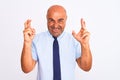 Middle age businessman wearing tie standing over isolated white background gesturing finger crossed smiling with hope and eyes