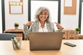 Middle age businesswoman sitting on desk working using laptop at office looking confident with smile on face, pointing oneself Royalty Free Stock Photo