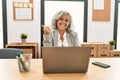 Middle age businesswoman sitting on desk working using laptop at office smiling with happy face looking and pointing to the side Royalty Free Stock Photo