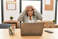 Middle age businesswoman sitting on desk working using laptop at office suffering from headache desperate and stressed because Royalty Free Stock Photo