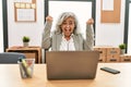 Middle age businesswoman sitting on desk working using laptop at office very happy and excited doing winner gesture with arms Royalty Free Stock Photo