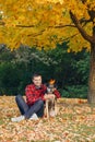 Middle age Caucasian bearded man sitting on ground among autumn fall yellow leaves and hugging pet dog Royalty Free Stock Photo
