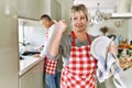Middle age caucasian couple wearing apron washing dishes at home pointing thumb up to the side smiling happy with open mouth Royalty Free Stock Photo