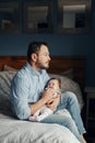 Middle age Caucasian father holding rocking newborn baby on laps. Tired man parent sitting on bed at home with a child on arms