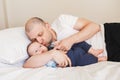 middle age Caucasian father in white t-shirt lying in bed with newborn baby son Royalty Free Stock Photo