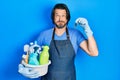 Middle age caucasian man holding cleaning products and cockroach puffing cheeks with funny face