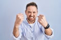 Middle age caucasian man standing over blue background angry and mad raising fists frustrated and furious while shouting with Royalty Free Stock Photo