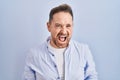 Middle age caucasian man standing over blue background angry and mad screaming frustrated and furious, shouting with anger Royalty Free Stock Photo