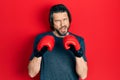 Middle age caucasian man using boxing gloves in shock face, looking skeptical and sarcastic, surprised with open mouth Royalty Free Stock Photo