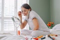 Middle age Caucasian woman applying her makeup in morning and talking over phone. Young woman sitting in bed at home bedroom doing Royalty Free Stock Photo