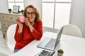 Middle age caucasian woman holding piggy bank sitting on the table at home Royalty Free Stock Photo