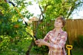 Middle age caucasian woman sprays trees against pests, vermin or diseases plants. Seasonal working in garden