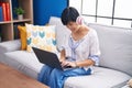 Middle age chinese woman using laptop and headphones sitting on sofa at home Royalty Free Stock Photo