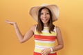 Middle age chinese woman wearing summer hat over yellow background smiling cheerful presenting and pointing with palm of hand Royalty Free Stock Photo