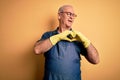 Middle age cleaner man cleaning wearing apron and gloves over isolated yellow background smiling in love showing heart symbol and