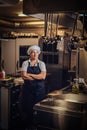 A middle age cook wearing a uniform standing with her arms crossed at restaurant`s kitchen. Royalty Free Stock Photo