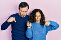 Middle age couple of hispanic woman and man holding keys of new home pointing down looking sad and upset, indicating direction