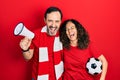 Middle age couple of hispanic woman and man wearing team scarf cheering game holding megaphone and ball smiling and laughing hard Royalty Free Stock Photo