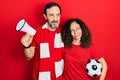 Middle age couple of hispanic woman and man wearing team scarf cheering game holding megaphone and ball smiling looking to the Royalty Free Stock Photo