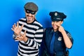 Middle age couple of hispanic woman and man wearing thief and police uniform pointing with hand finger to face and nose, smiling