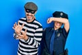 Middle age couple of hispanic woman and man wearing thief and police uniform smiling cheerful playing peek a boo with hands