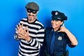 Middle age couple of hispanic woman and man wearing thief and police uniform smiling doing phone gesture with hand and fingers