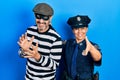 Middle age couple of hispanic woman and man wearing thief and police uniform smiling friendly offering handshake as greeting and