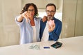 Middle age couple holding piggy bank calculating savings with angry face, negative sign showing dislike with thumbs down, Royalty Free Stock Photo