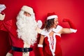 Middle age couple wearing Santa costume and glasses over isolated red background showing arms muscles smiling proud Royalty Free Stock Photo